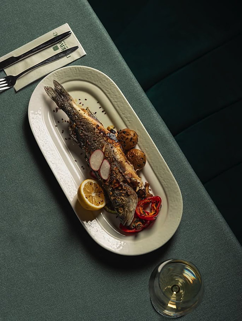 Whole grilled sea bass on the table at Melaverde, Novobërdë